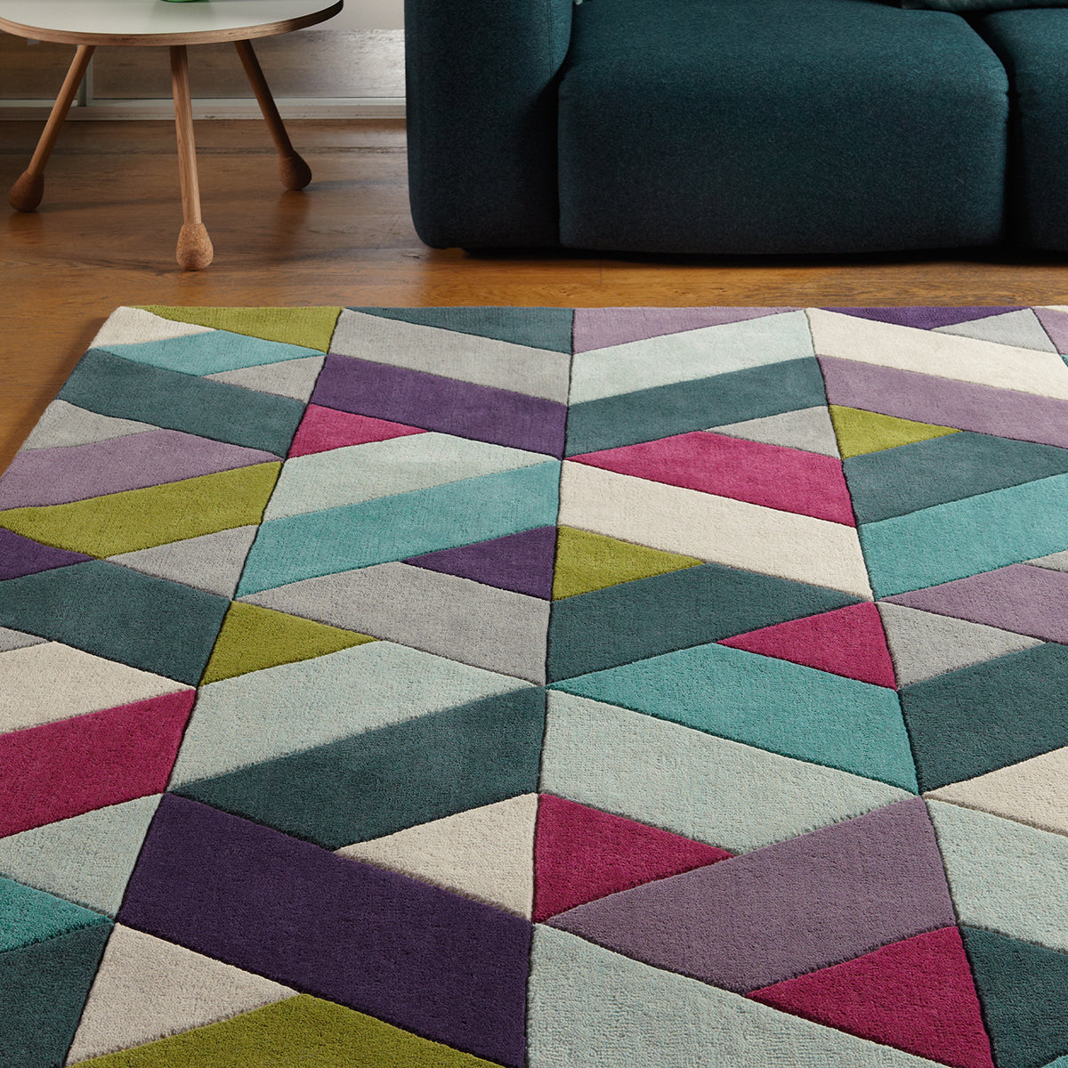 Multicolored geometric patterned rug on a wooden floor with a teal sofa in the background.