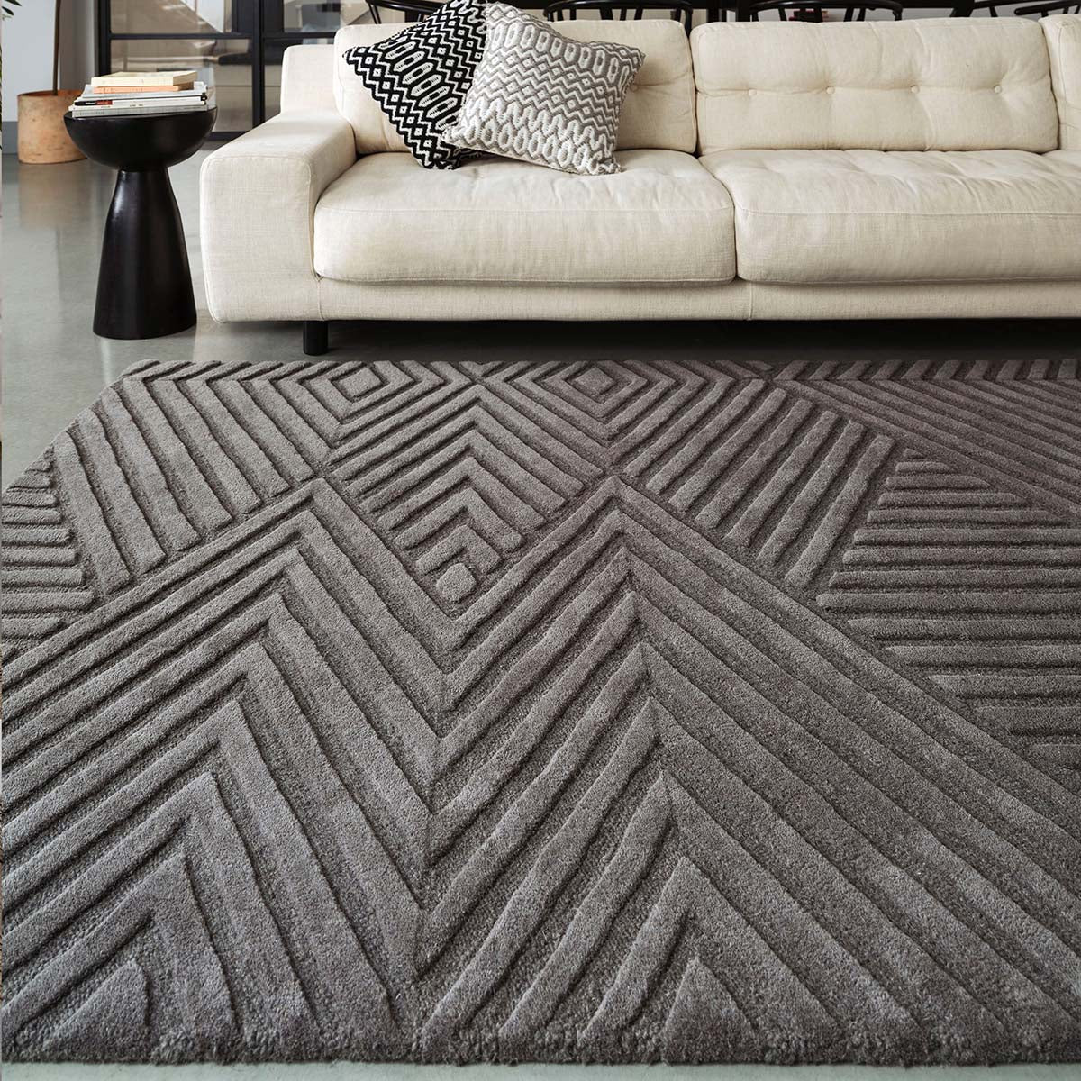 Gray geometric-patterned rug in front of a beige sofa with patterned cushions.