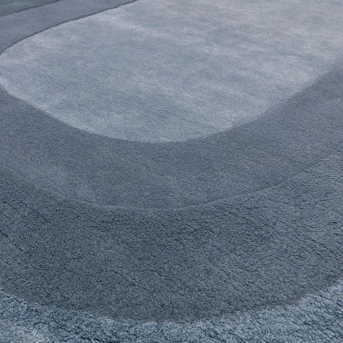 Asiatic Halo Denim Oval Rug featuring halo circular pattern in denim blue, navy and light blue on blue-grey background, hand-tufted wool