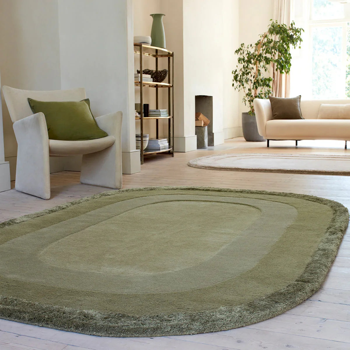 Green oval rug in a living room with a beige sofa, white chair, and bookshelf.