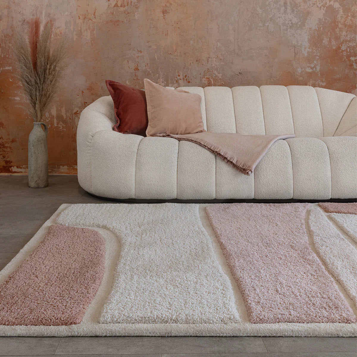 Beige sofa with pink and red cushions in a room with a textured wall and patterned rug.