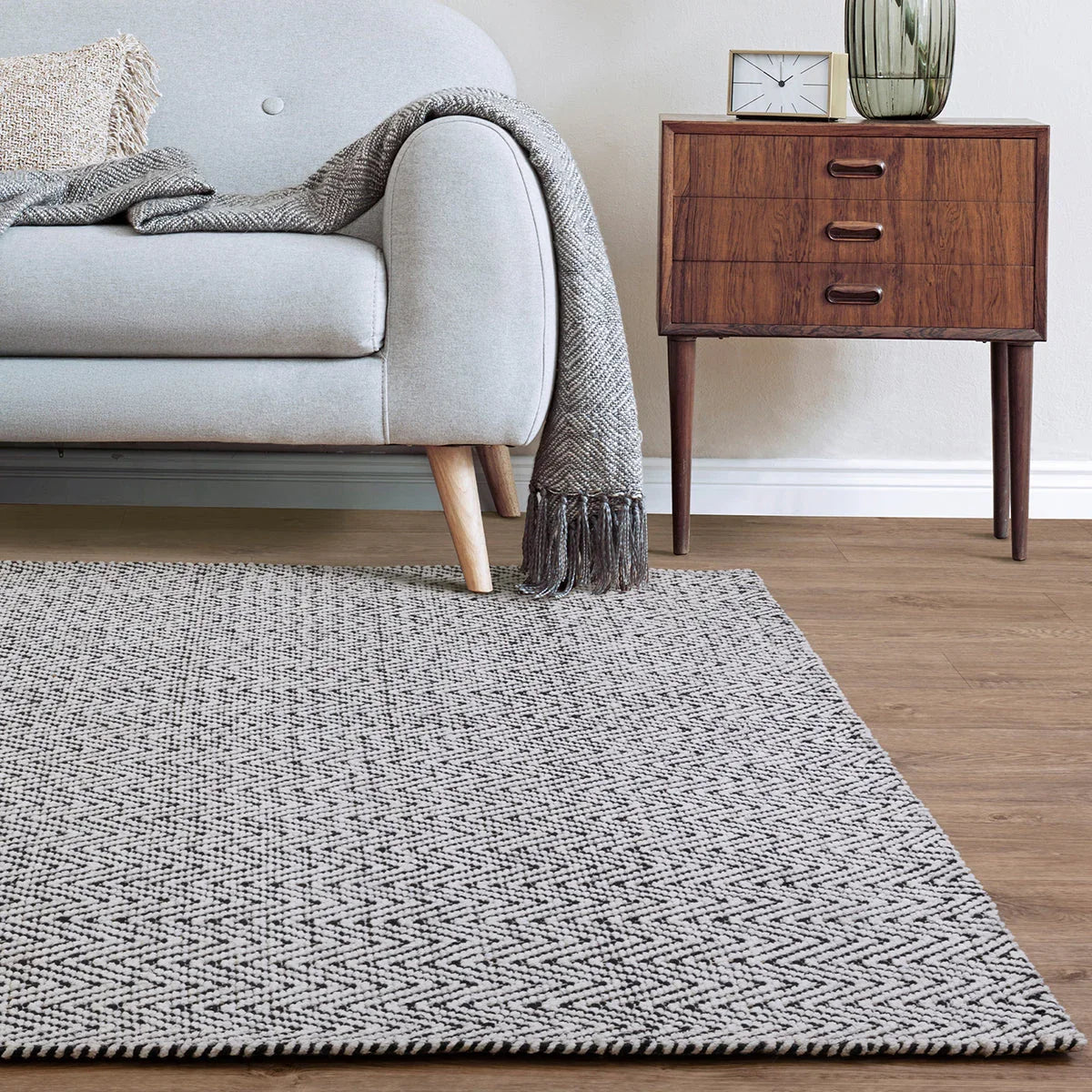 Gray textured rug in a living room with a sofa and wooden side table.