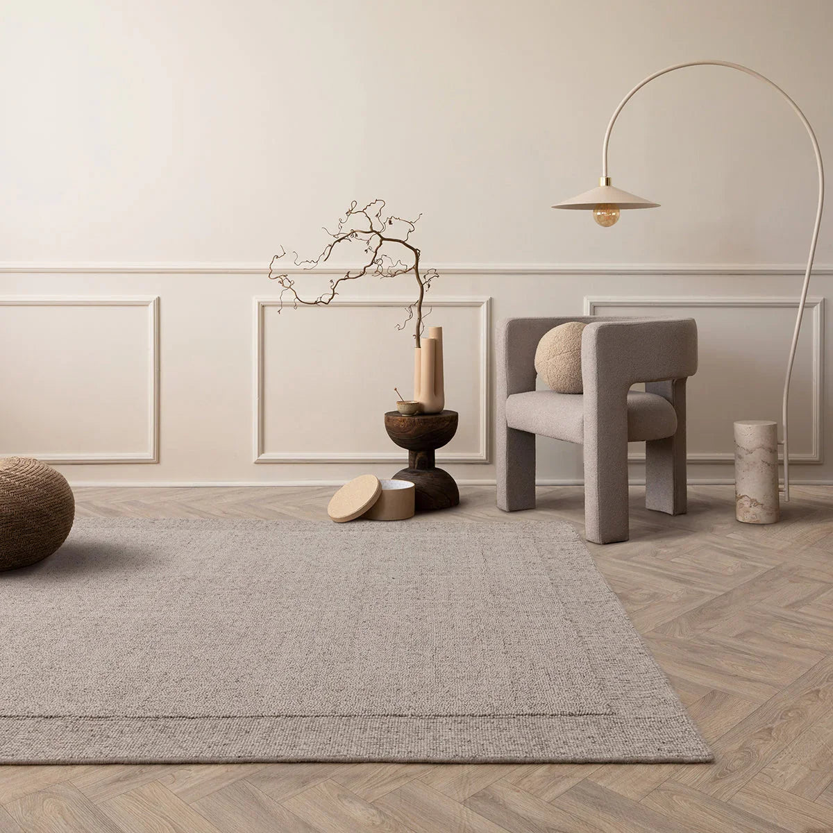 Modern interior with a gray rug, chair, and decorative items on a wooden floor.