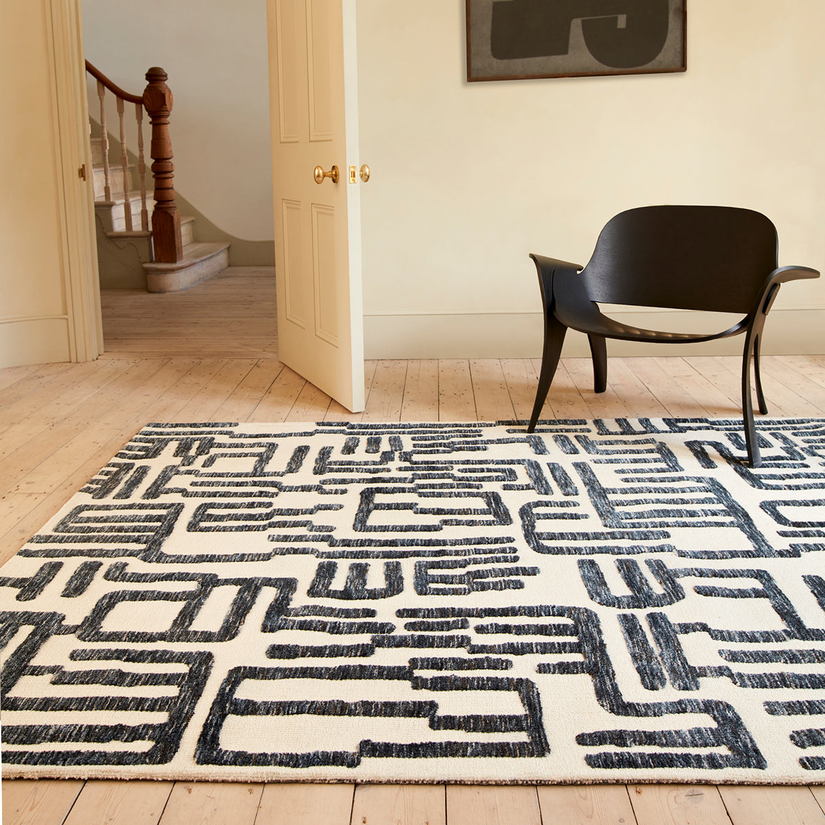 Patterned rug on a wooden floor with a black chair and staircase in the background.
