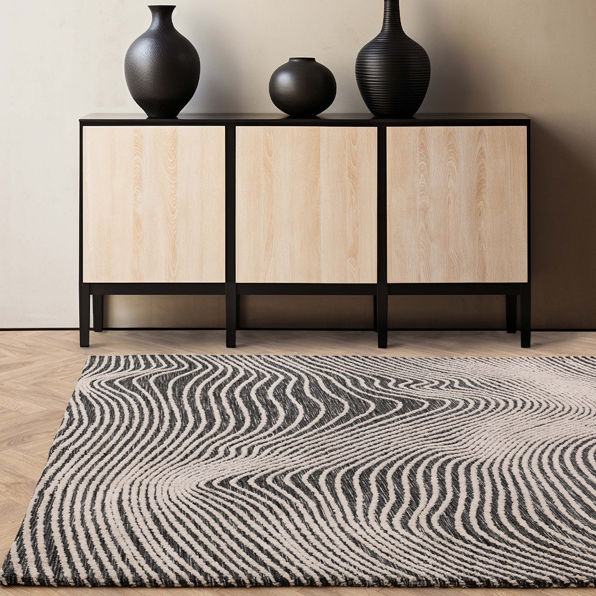 Rug with wavy pattern in front of a wooden cabinet with black frames and vases.