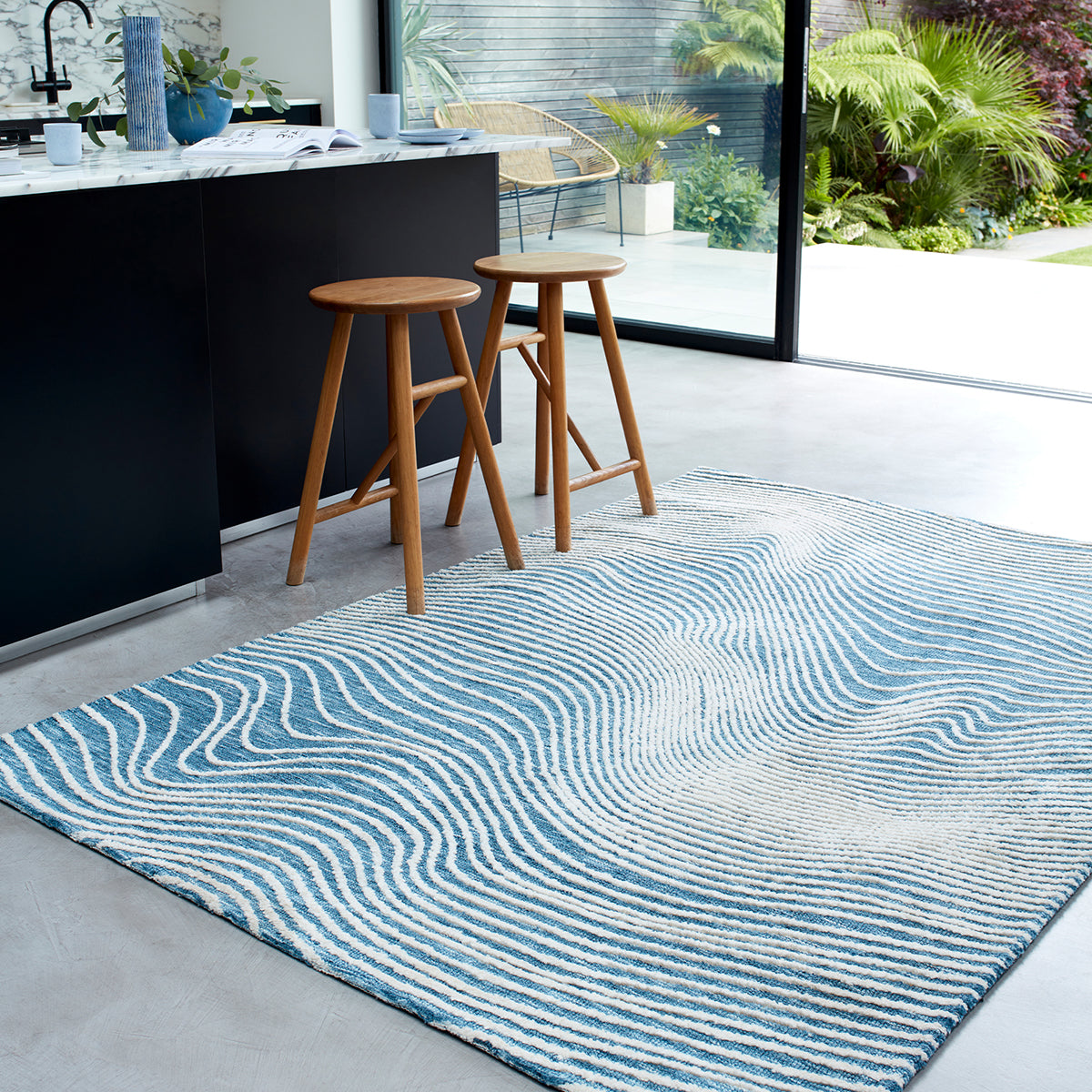 Blue and white patterned rug on a gray floor with wooden stools in a modern kitchen.