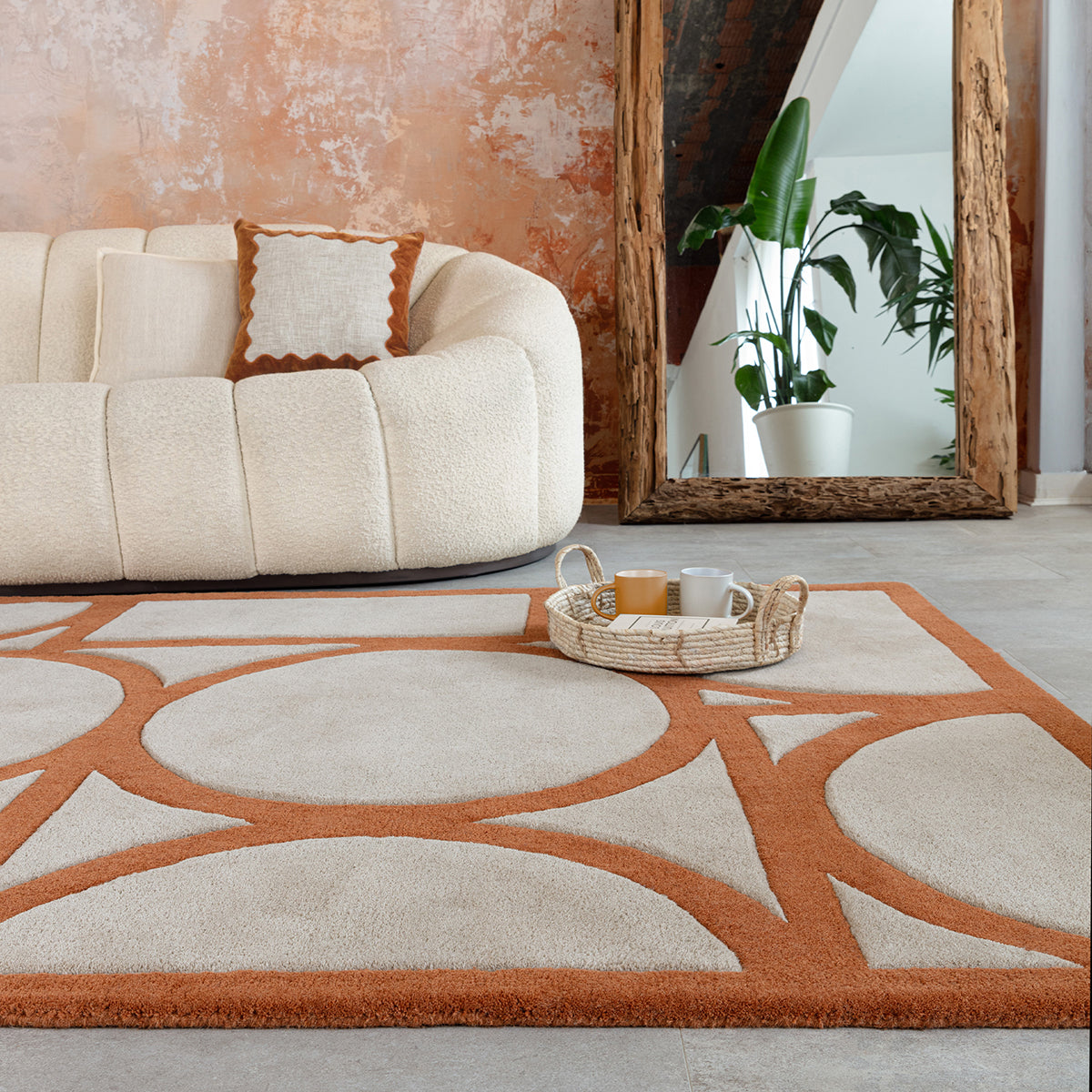 Living room with a beige and orange patterned rug, white sofa, and decorative mirror.