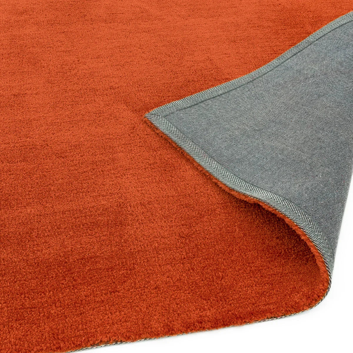 Asiatic Milo Rust Designer Rug featuring solid rust-orange field with grey-blue underside in a herringbone border on white background, hand-tufted wool