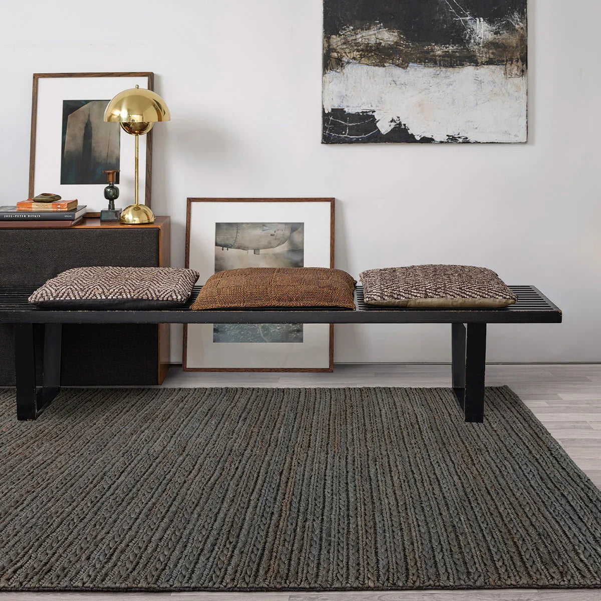 Living room with a black bench, textured rug, and framed artwork on a white wall.
