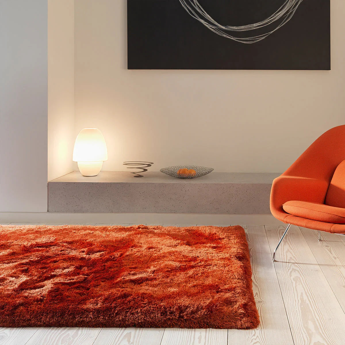 Modern living room with a red rug, orange chair, and abstract art on the wall.