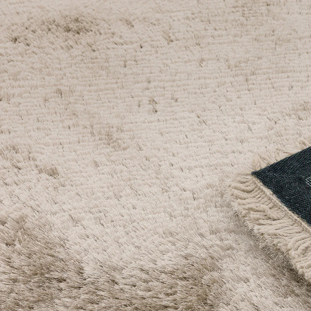 Asiatic Plush Sand Round Designer Rug featuring plush shag in sand, cream and taupe with dark indigo edge on beige background, hand-tufted wool