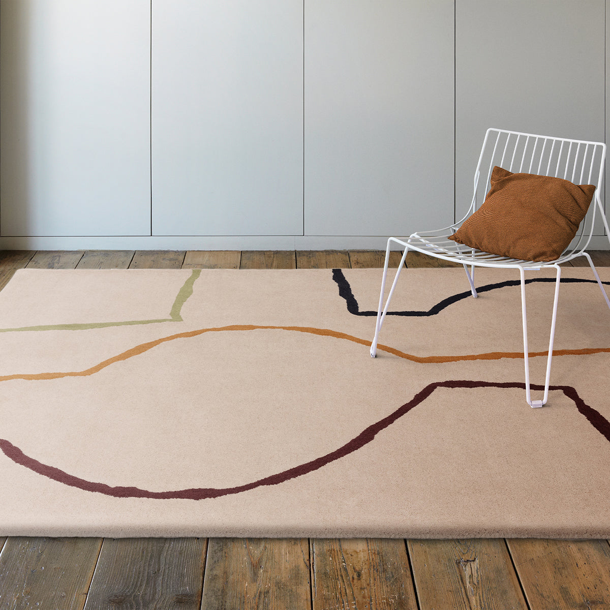 Beige rug with abstract line design in a room with a white chair and brown pillow.