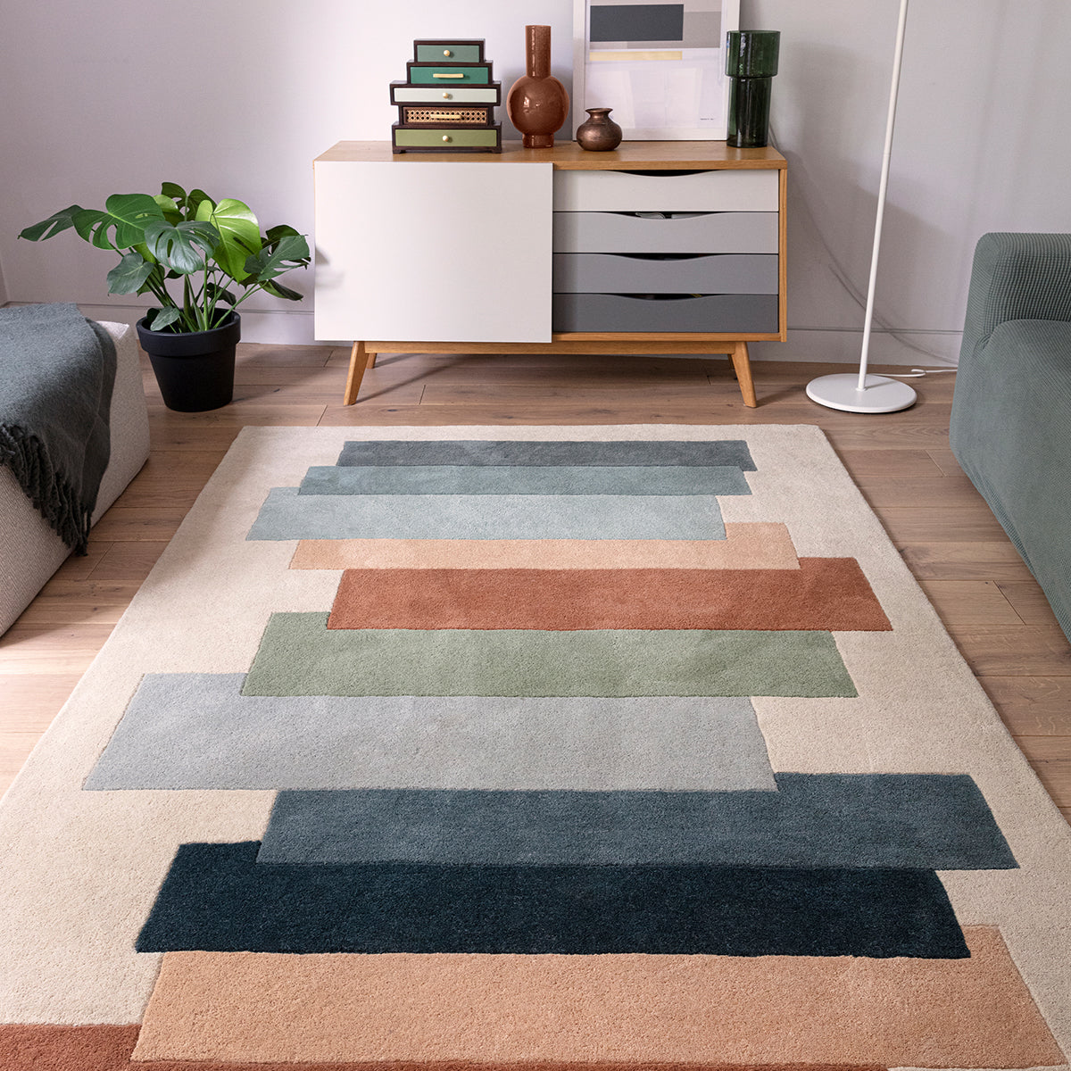 Colorful geometric rug on a wooden floor with a sideboard and plant in the background.