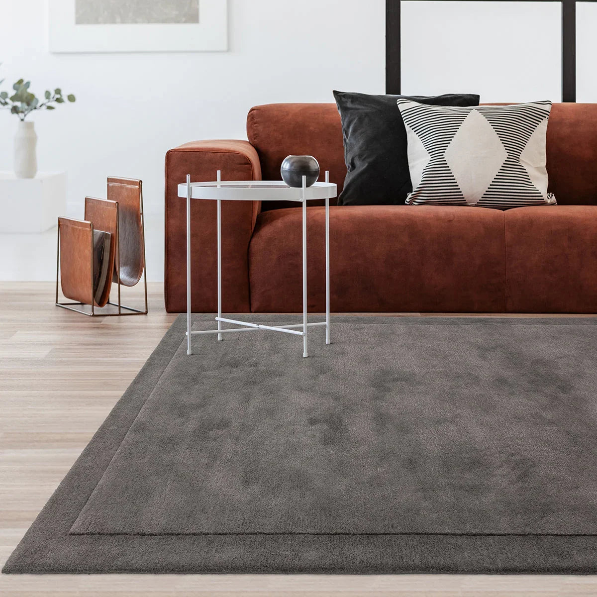 Living room with a brown sofa, gray rug, and side table.