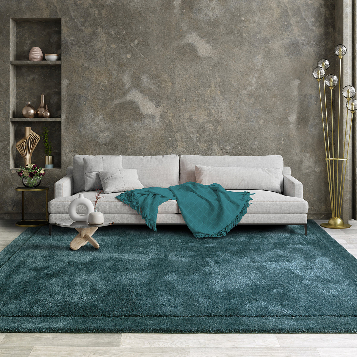 Gray sofa with a teal blanket on a teal rug in a modern living room.