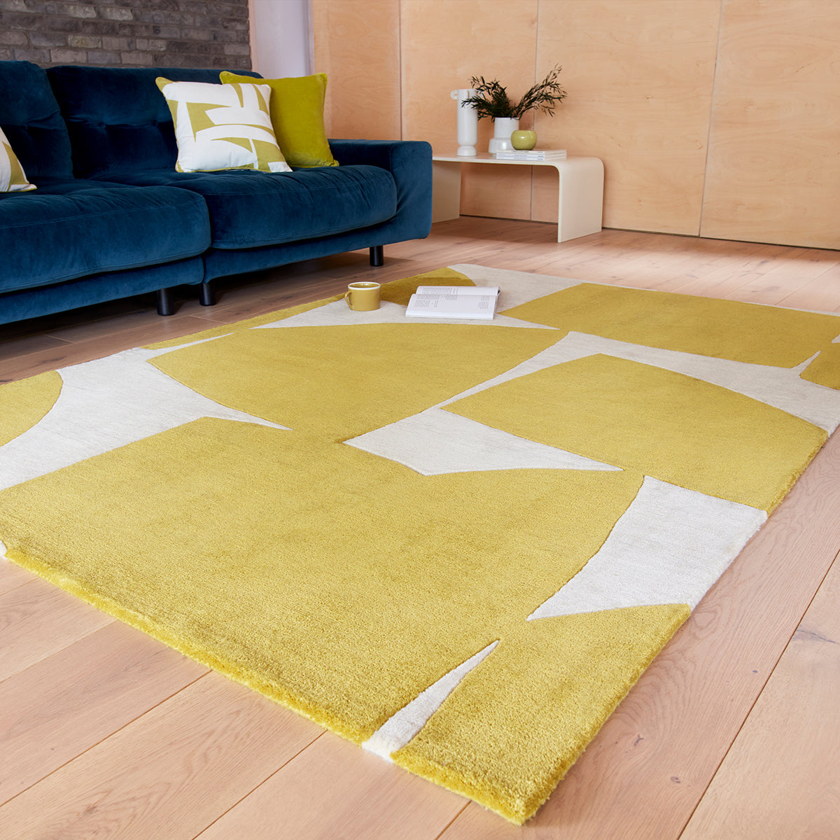 Yellow geometric rug on a wooden floor with a blue sofa and decorative items in the background.