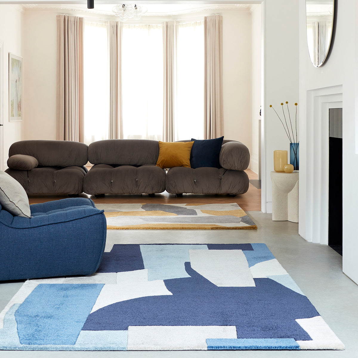 Modern living room with a brown sofa, blue armchair, and a colorful geometric rug.
