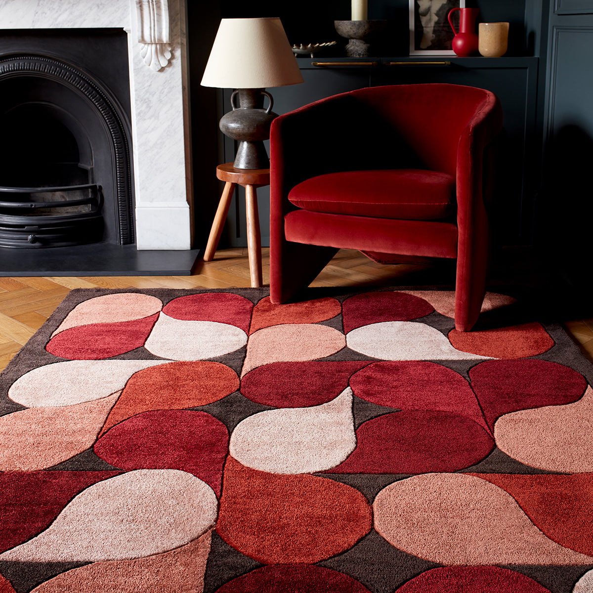 Red armchair on a patterned rug in a living room with a fireplace.