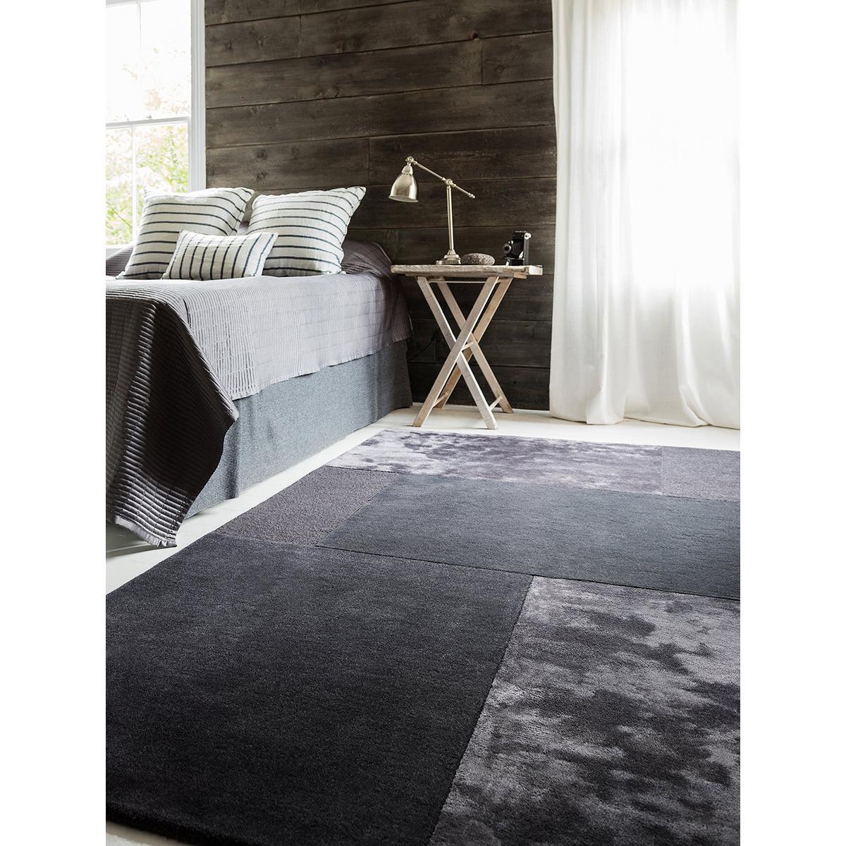 Modern bedroom with a dark gray rug, bed, and side table.