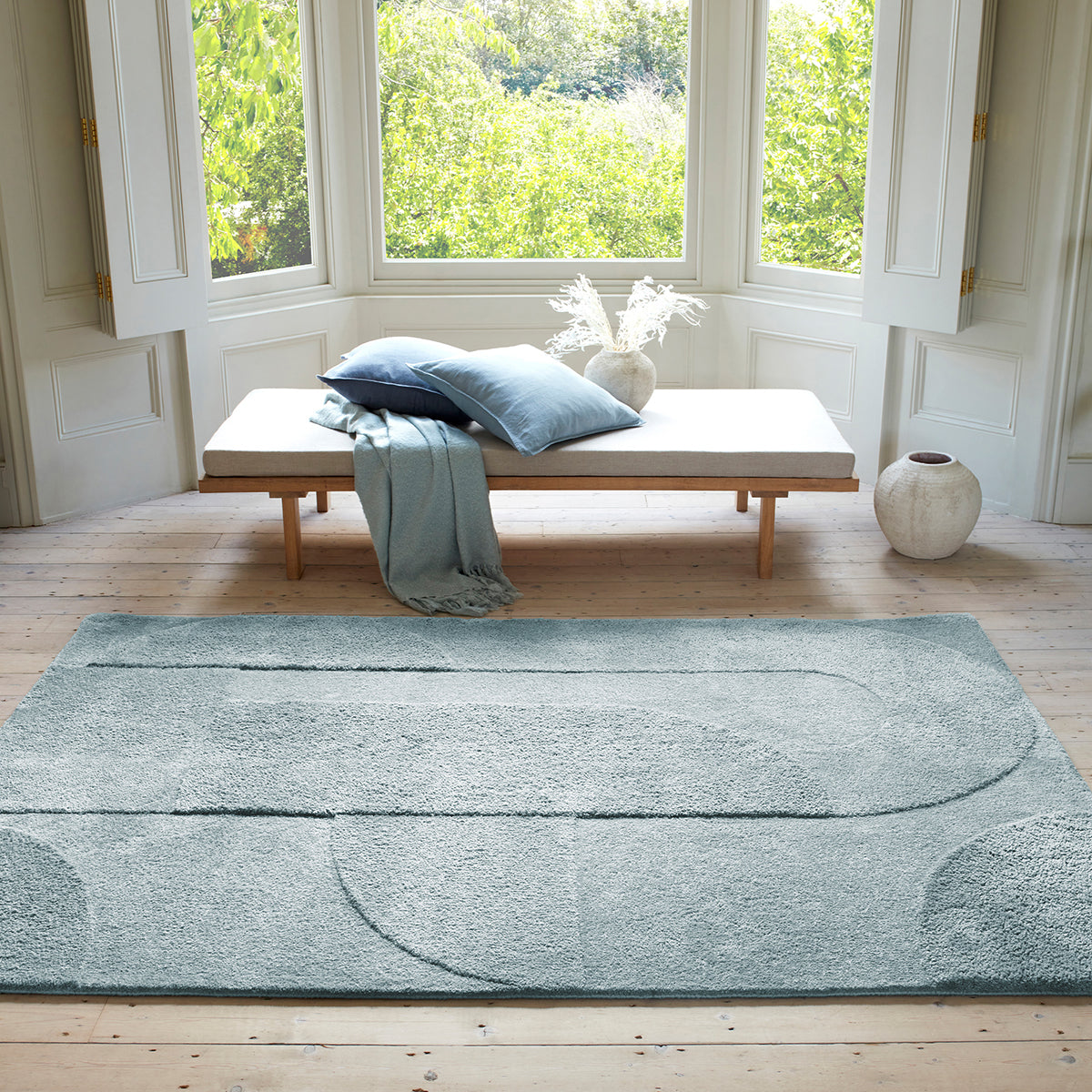 Light blue rug on a wooden floor with a bench and pillows in the background.