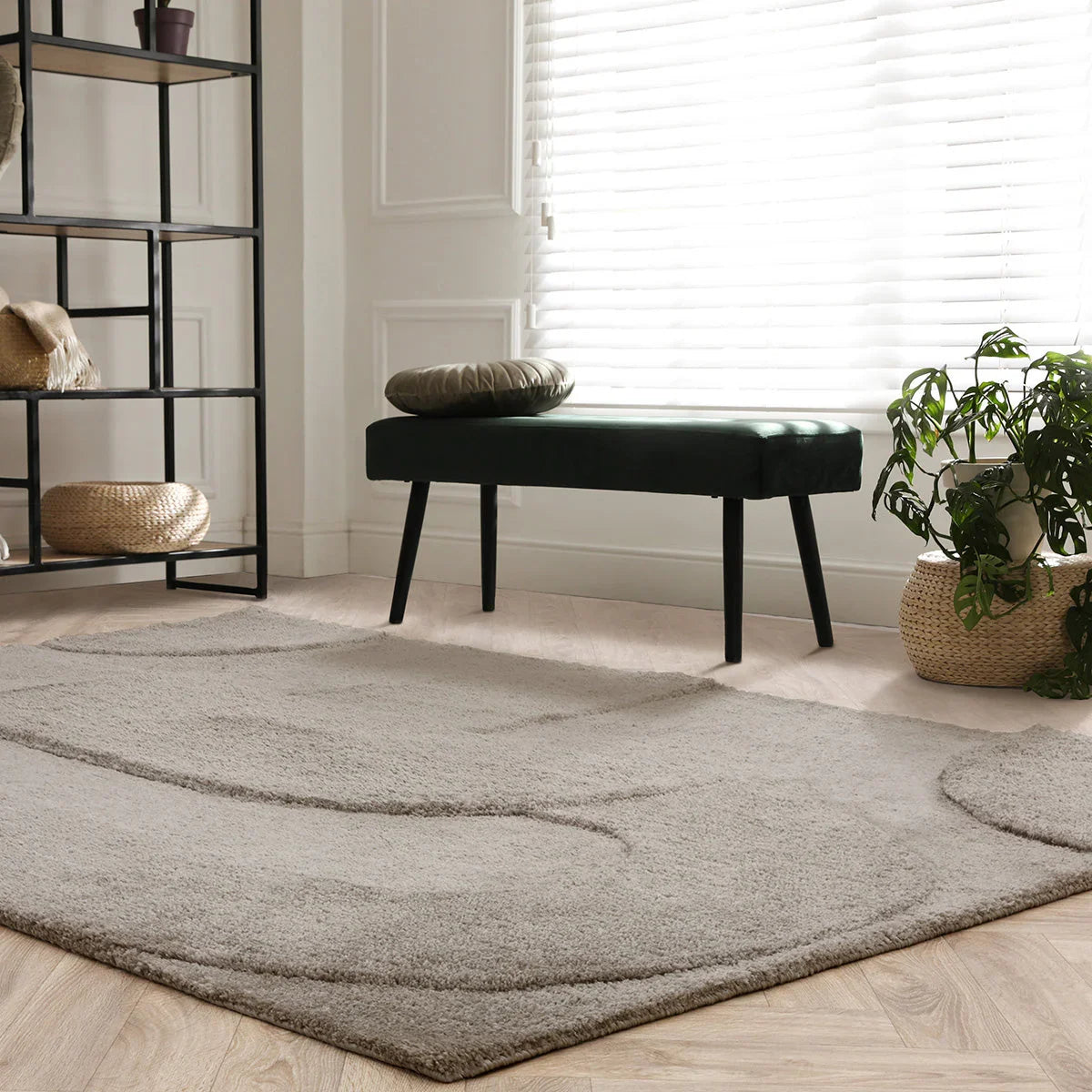 Gray rug on a wooden floor with a black bench and plant in the background.