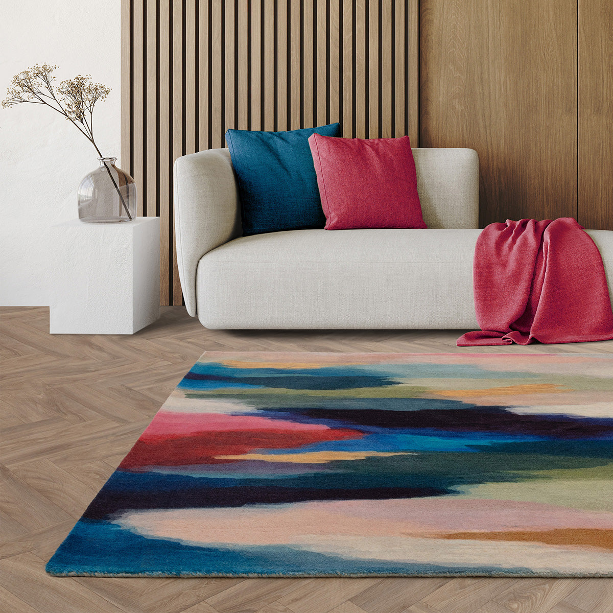 Colorful abstract rug in front of a sofa with decorative pillows and a vase.