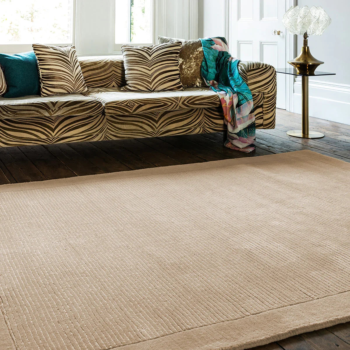 Beige rug in a living room with a patterned sofa and decorative pillows.