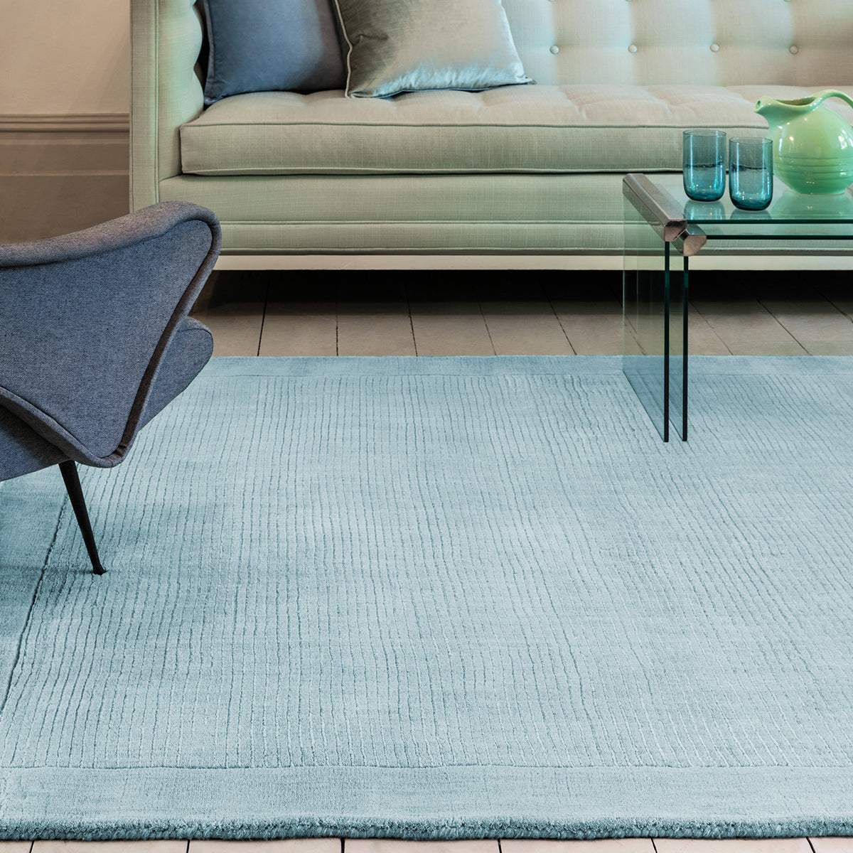 Living room with a light blue rug, gray chair, and beige sofa.