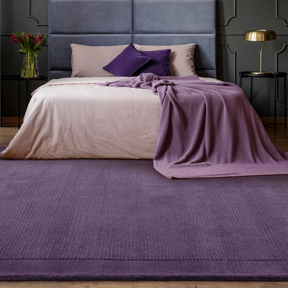 Bedroom with a bed featuring purple bedding and pillows, a purple rug, and decorative items.