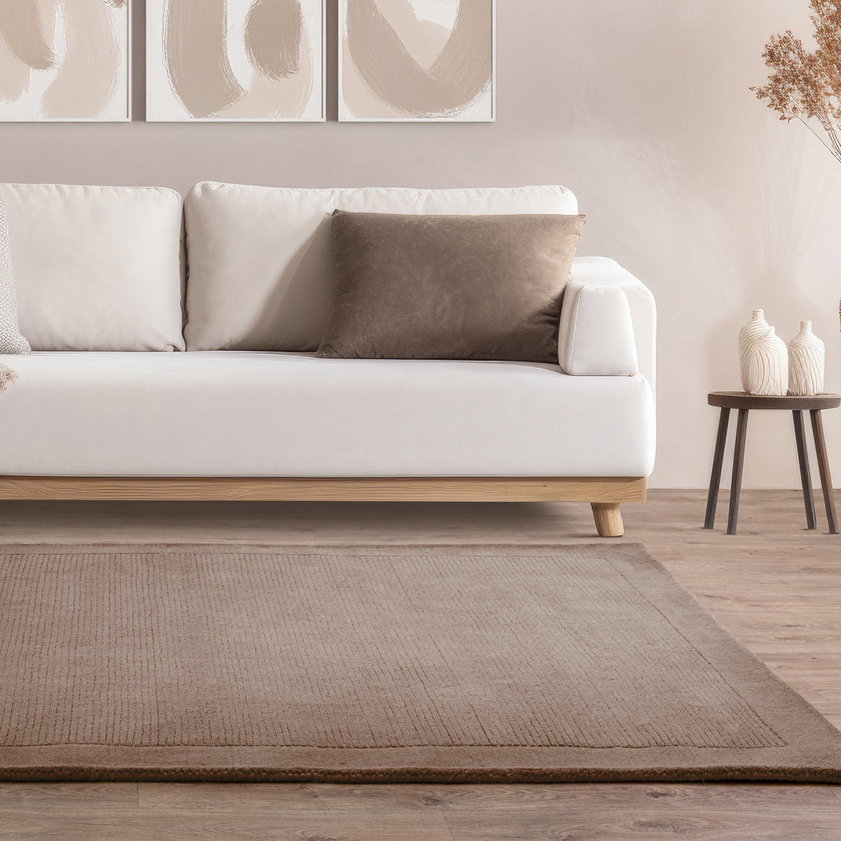 White sofa with a brown pillow in a living room setting with a beige rug and side table.