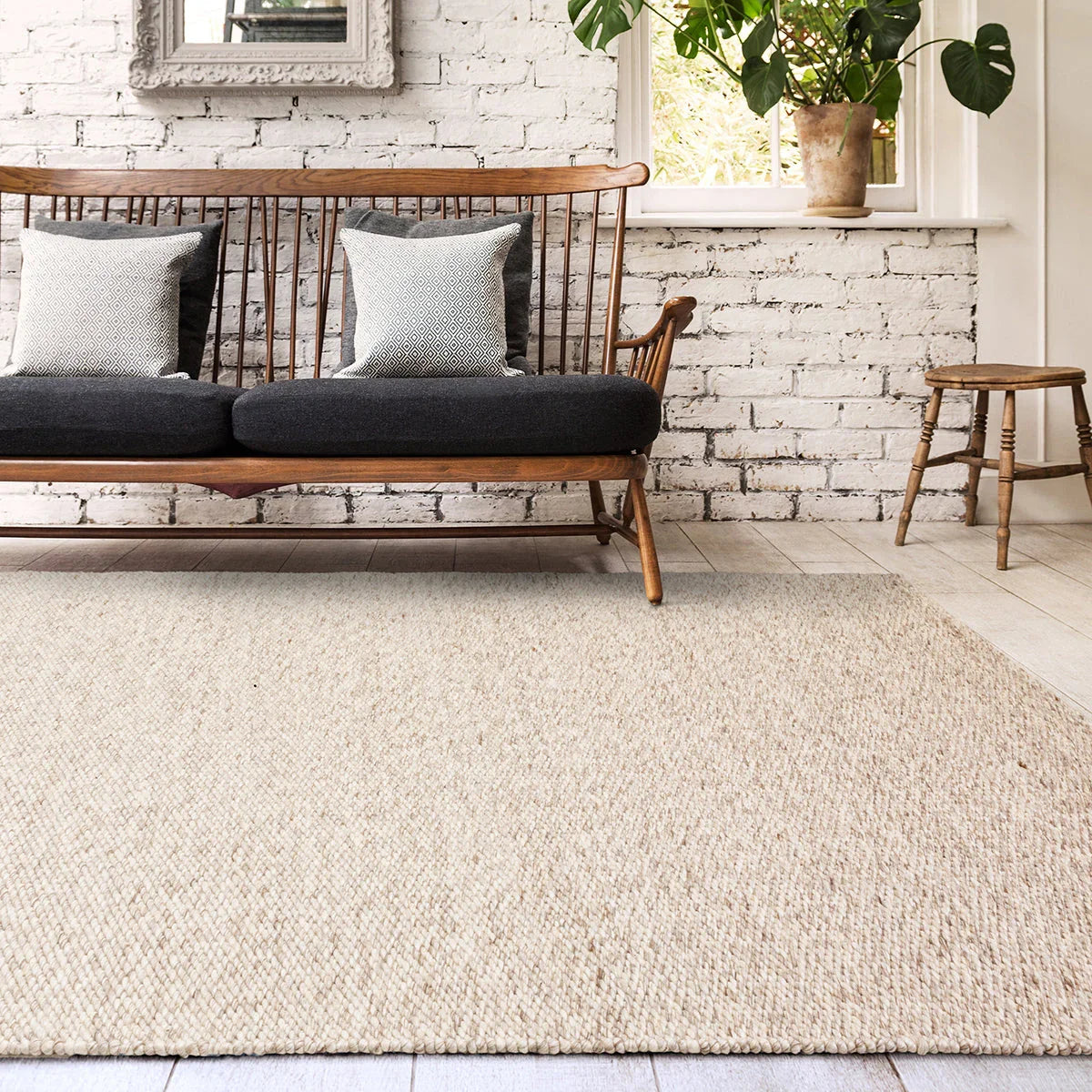 Wooden bench with cushions on a textured rug in a room with a white brick wall and a plant.