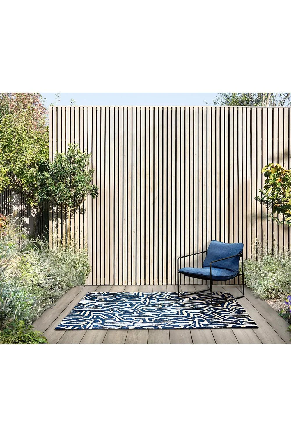 Harlequin Melodic Blue Designer Outdoor Rug featuring abstract wave pattern in navy blue, royal blue and ivory on light deck, outdoor-grade synthetic rug