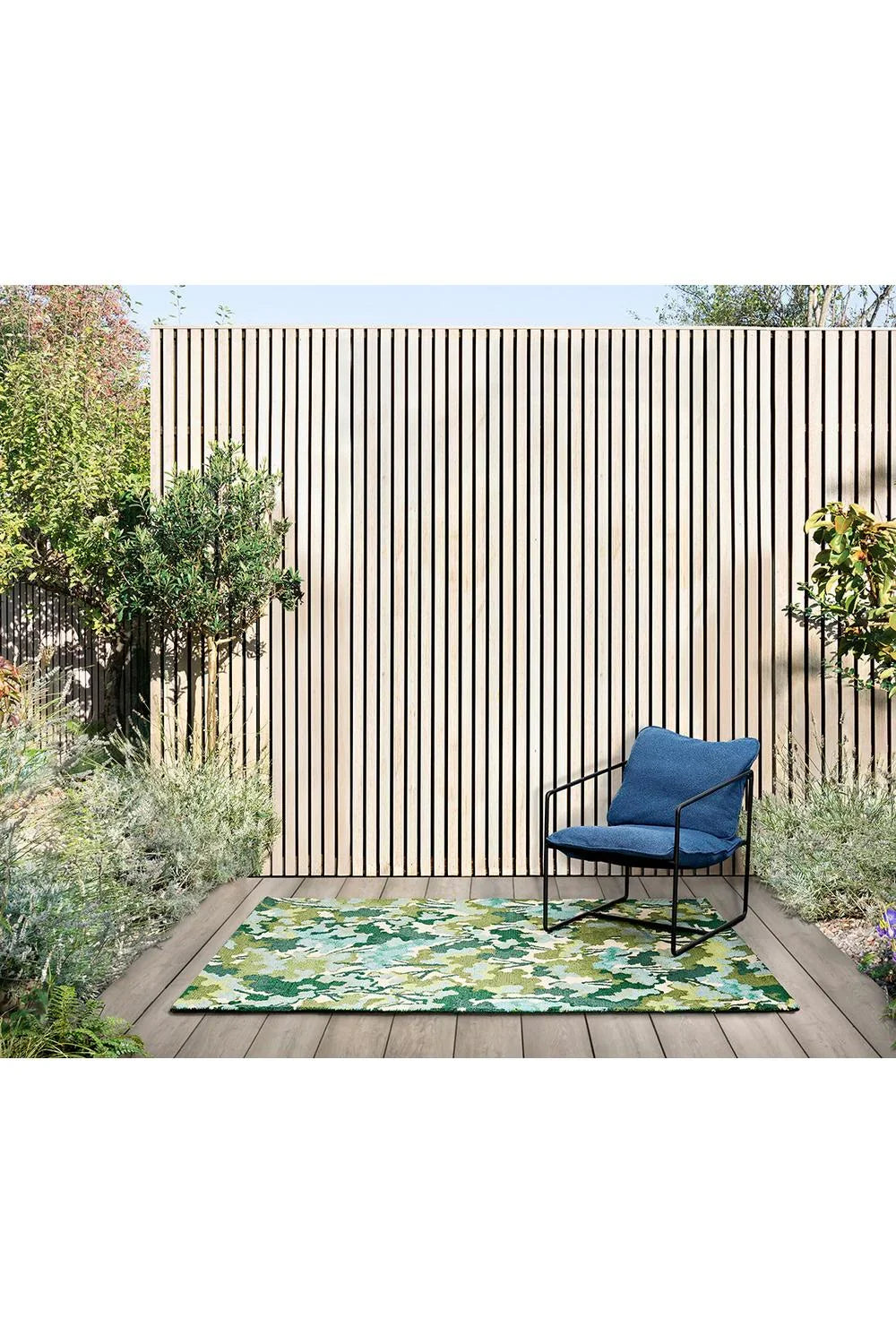 Harlequin Tree Tops Green Outdoor Rug featuring camo-inspired pattern in olive, lime, forest and cream on beige deck, machine-woven polypropylene