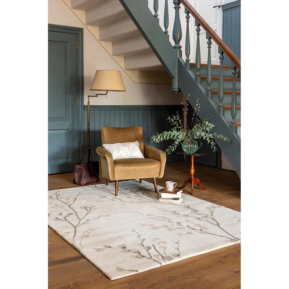 Laura Ashley Pussy Willow Dove Grey Designer Rug featuring botanical branch pattern in ivory, taupe and greige on warm brown wood floor, machine-woven wool