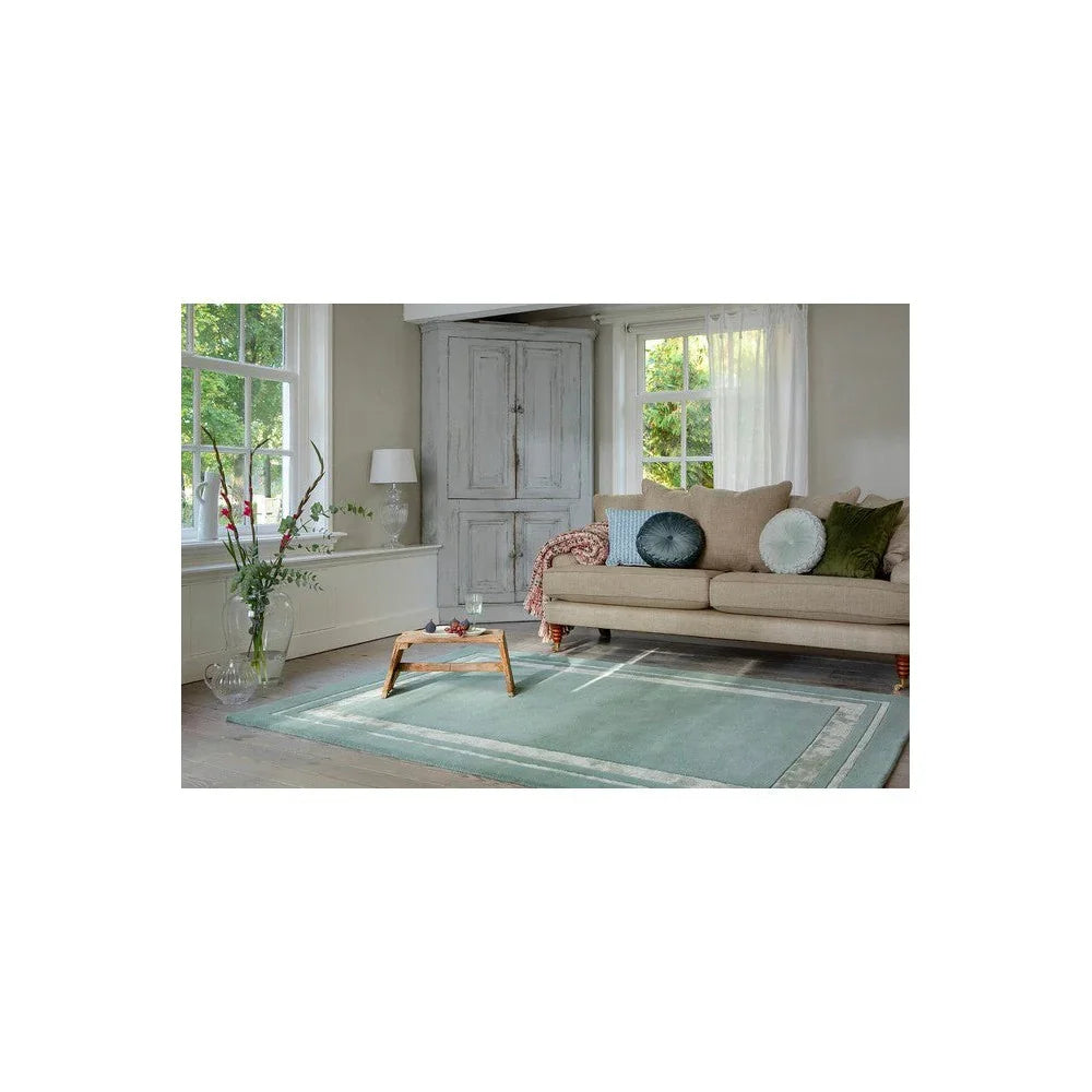 Laura Ashley Redbrook Duck Egg Designer Rug featuring a duck-egg blue bordered design in a bright living room.