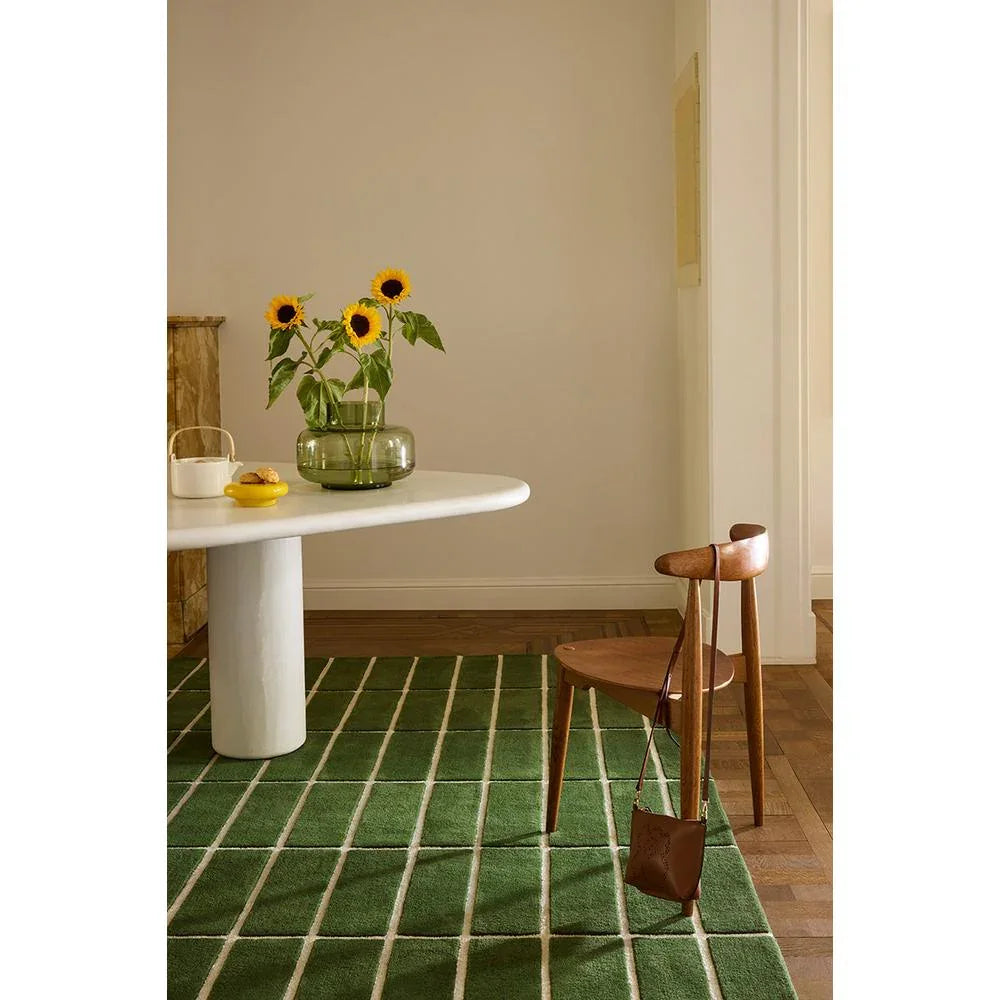 Marimekko Tiiliskivi Green 132907 Rug with geometric grid in green and white on brown wooden floor, machine-woven wool