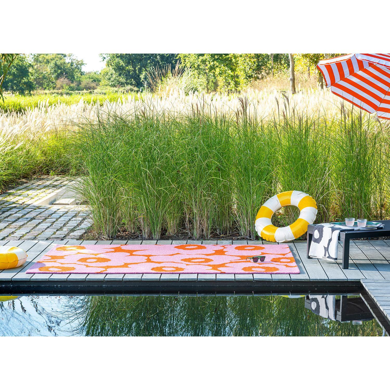 Marimekko Unikko Pink Orange Outdoor Rug featuring floral pattern in pink, orange on brown deck, woven polypropylene