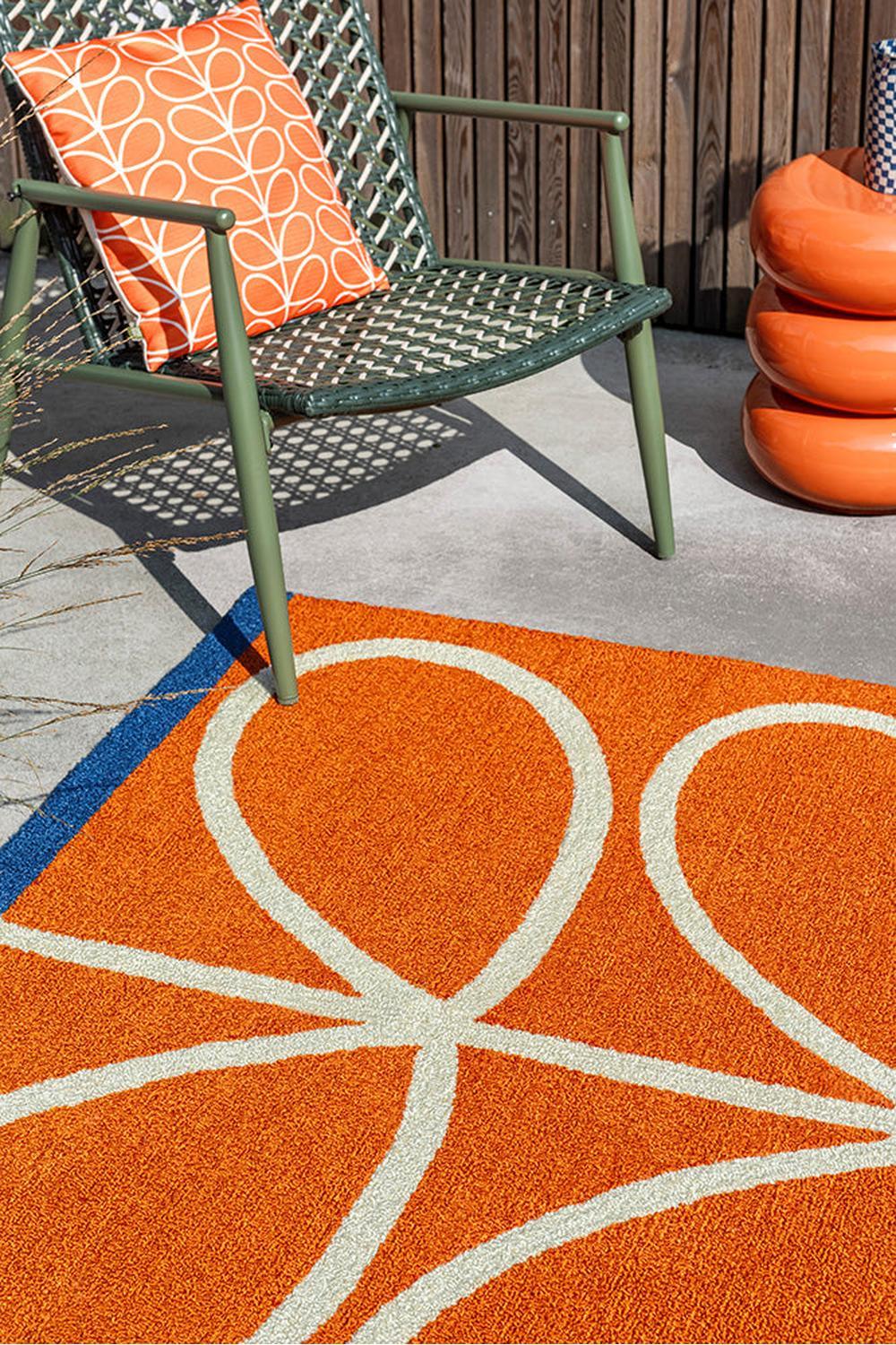 Orla Kiely Linear Stem Orange Outdoor Rug featuring looping stem pattern in orange and ivory on bright patio, machine-loomed polypropylene
