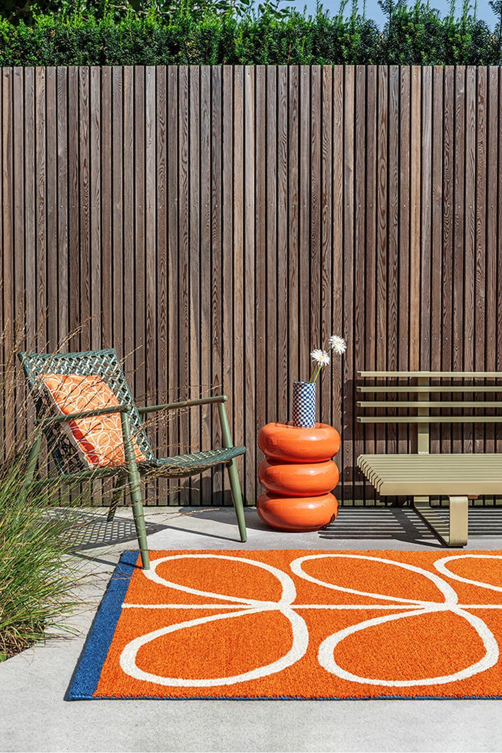 Orla Kiely Linear Stem Orange Outdoor Rug featuring orange/white stems with cobalt blue on light grey concrete, power-loomed polypropylene