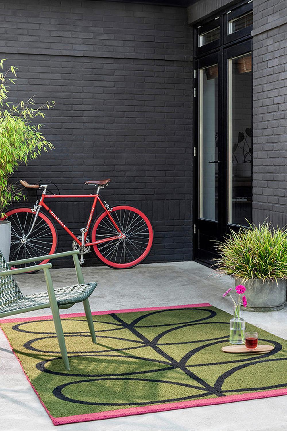 Orla Kiely Linear Stem Olive Outdoor Rug with abstract stem pattern in olive, black and pink on pink-edged olive field, machine-woven polypropylene