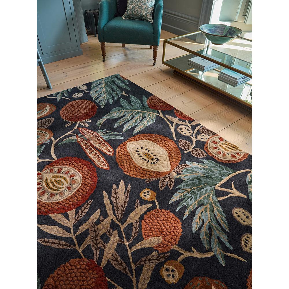 Sanderson Jackfruit Turmeric Indigo Rug featuring tropical fruit pattern in navy, turmeric, burnt orange, cream on dark navy background, hand-tufted wool