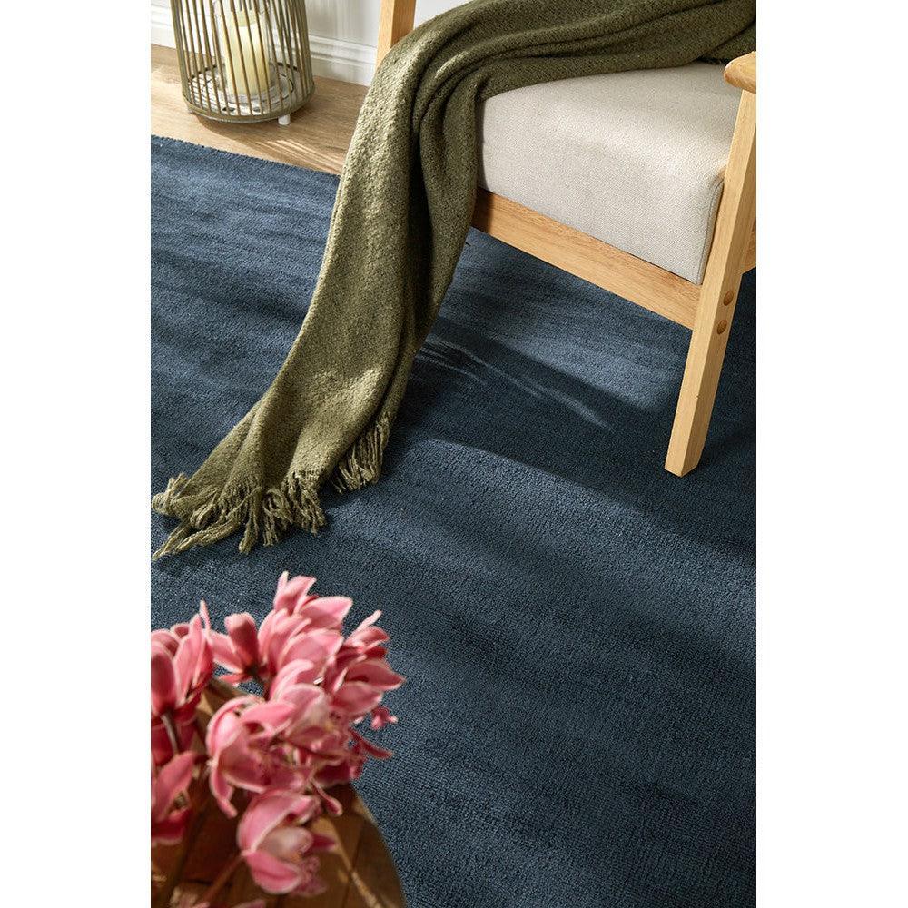 Joy Denim Rug featuring solid woven texture in denim blue, navy and slate on natural tan wooden floor, machine-made polyester