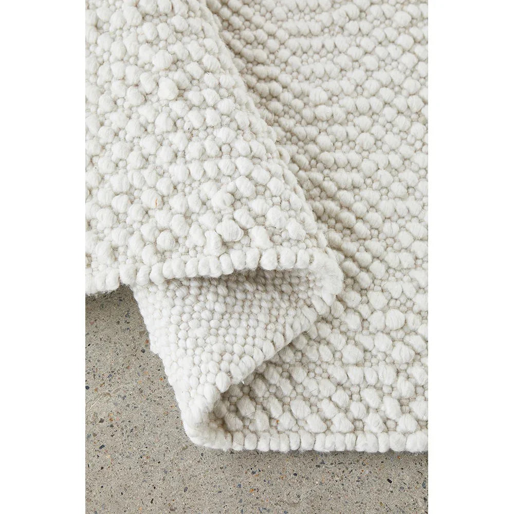 Boucle White Rug featuring chunky boucle texture in white and cream on light gray concrete, hand-tufted wool