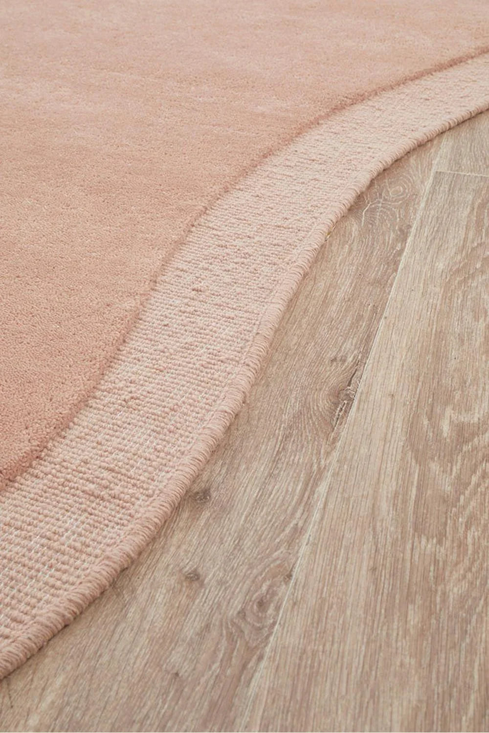 Cleo Blush Rug featuring solid blush pink pile with lighter border on light oak background, hand-tufted wool