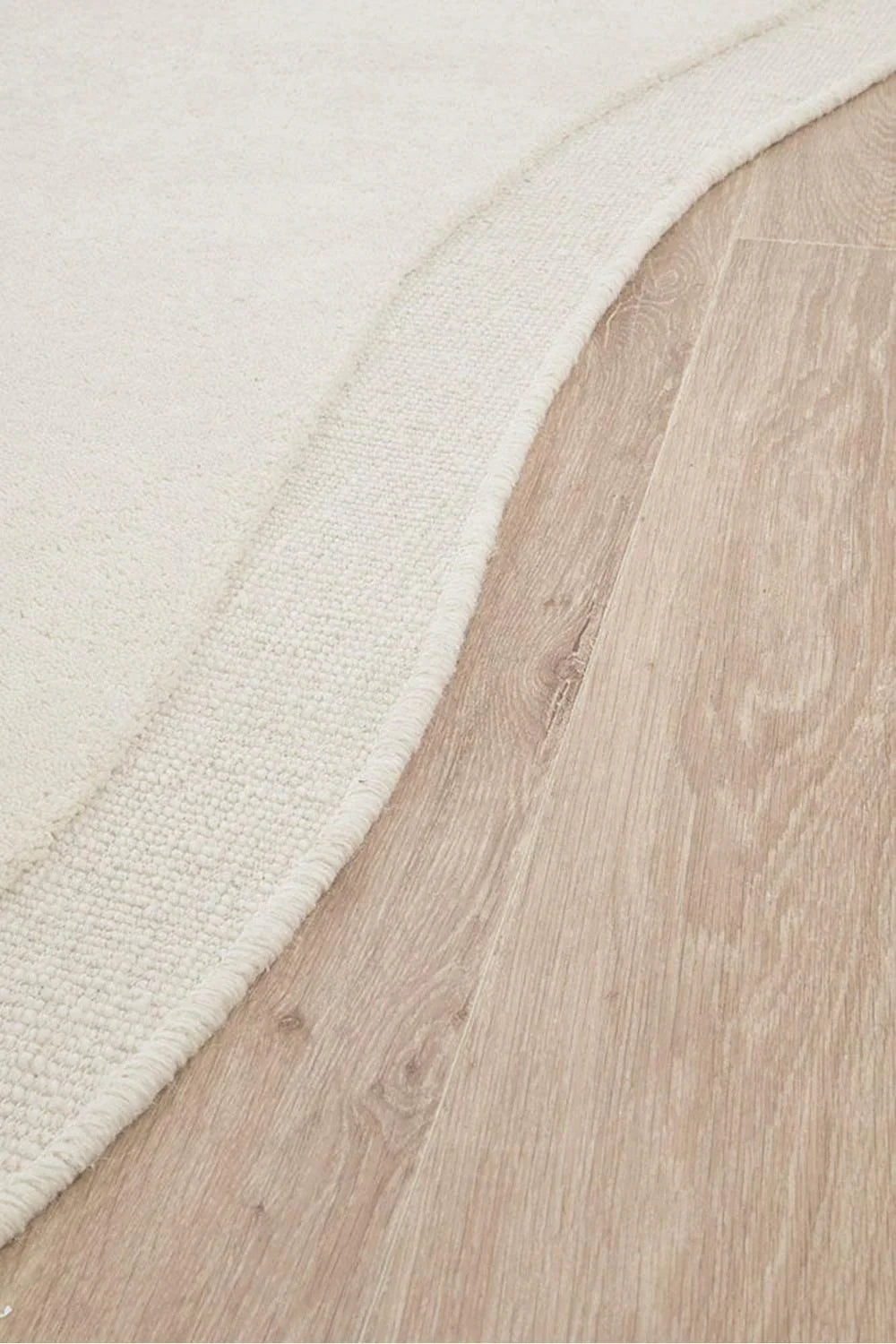 Cleo Milk Rug featuring soft curved silhouette in ivory and cream on light oak floor, woven wool