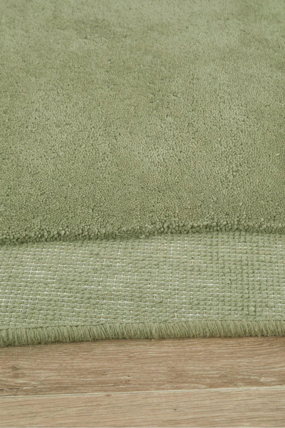 Cleo Moss Rug featuring solid plush moss-green pile on warm brown wooden floor, hand-tufted wool