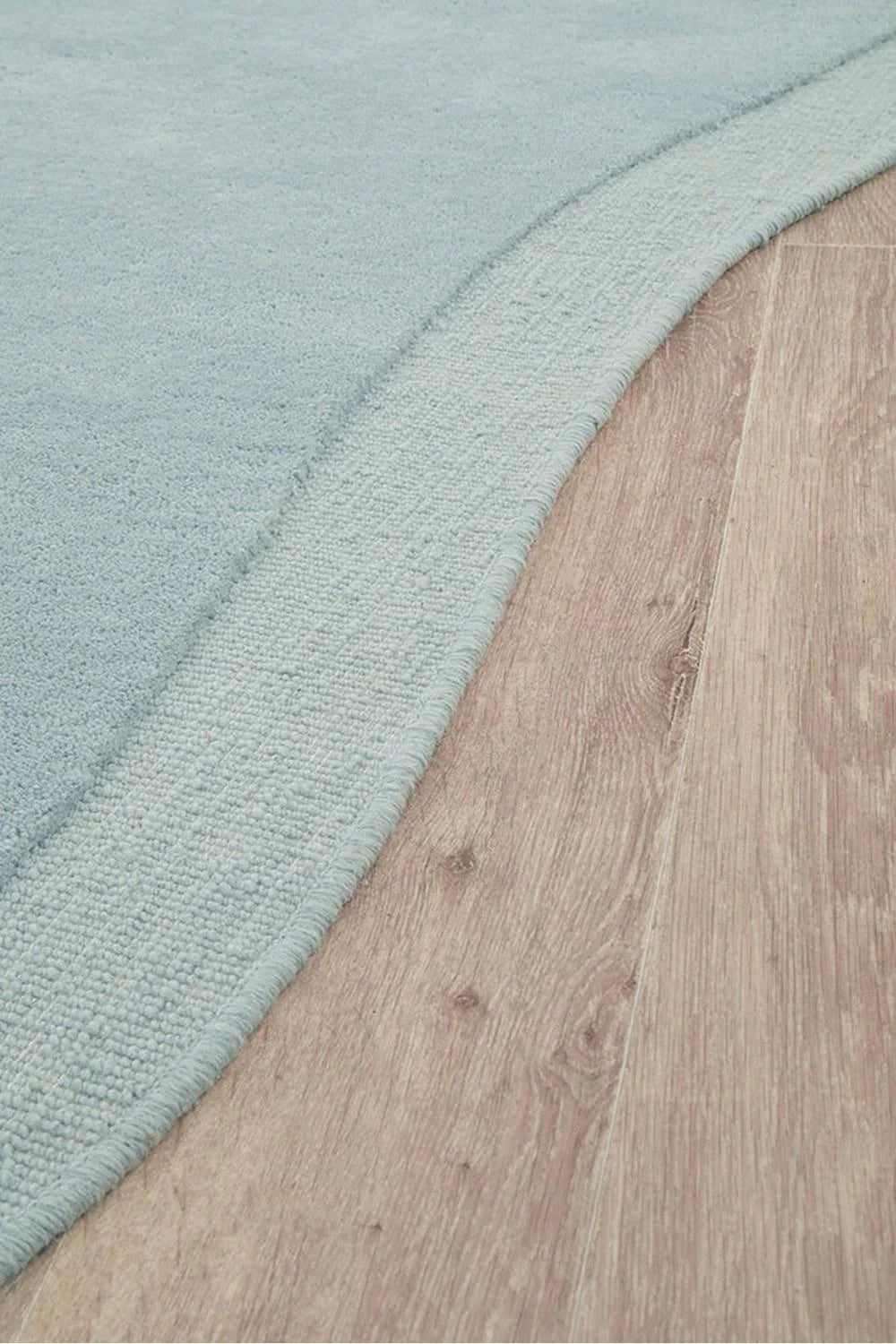 Cleo Sky Rug featuring solid texture in sky blue on warm tan wood background, hand-tufted wool