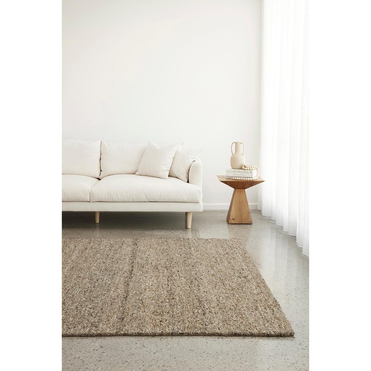 Conscious Loom Embrace Stone Rug featuring textured weave in stone, beige and ivory on pale grey floor, handwoven wool