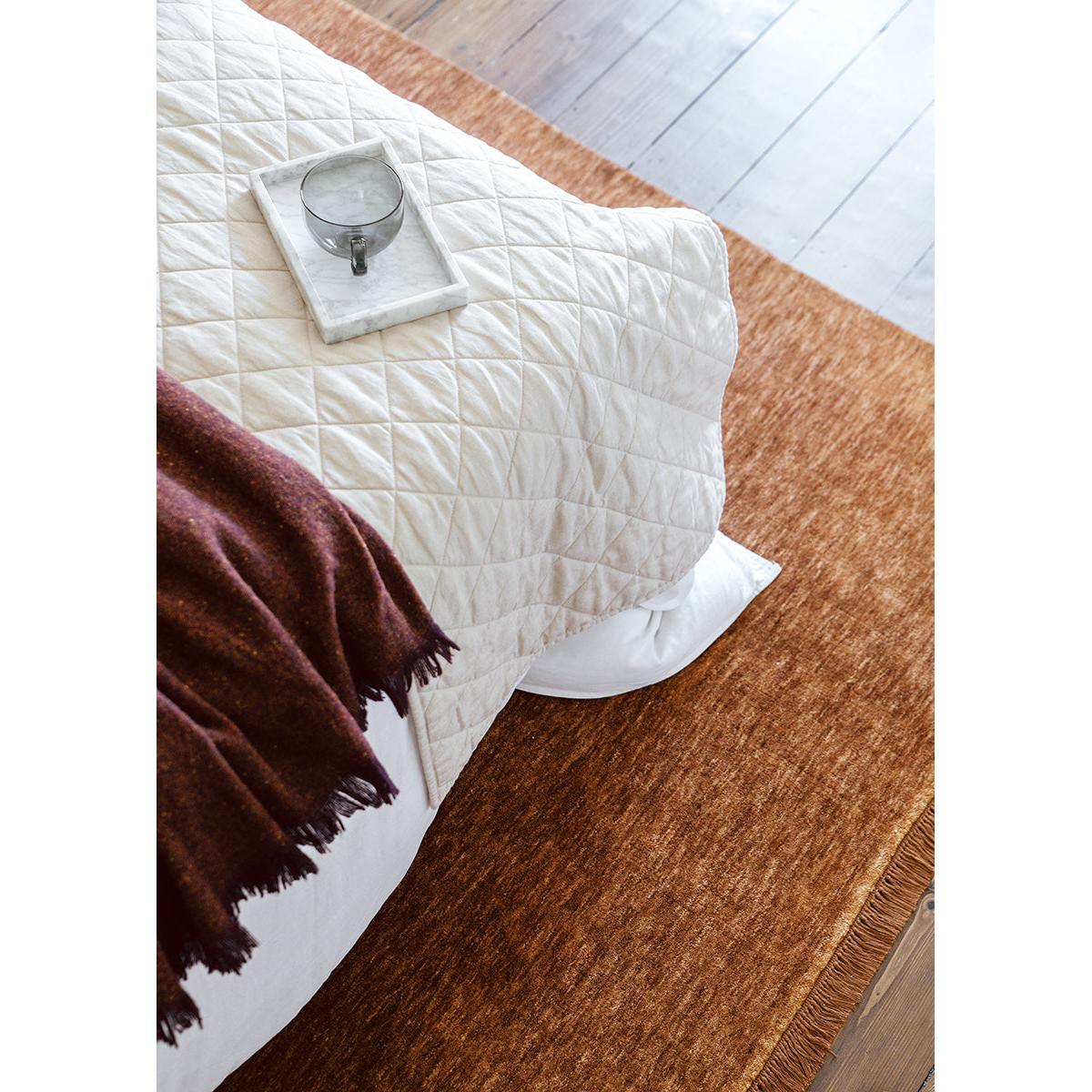 Conscious Loom Kinship Caramel Rug with textured pattern in caramel, copper and cream on brown floor, hand-loomed fibre