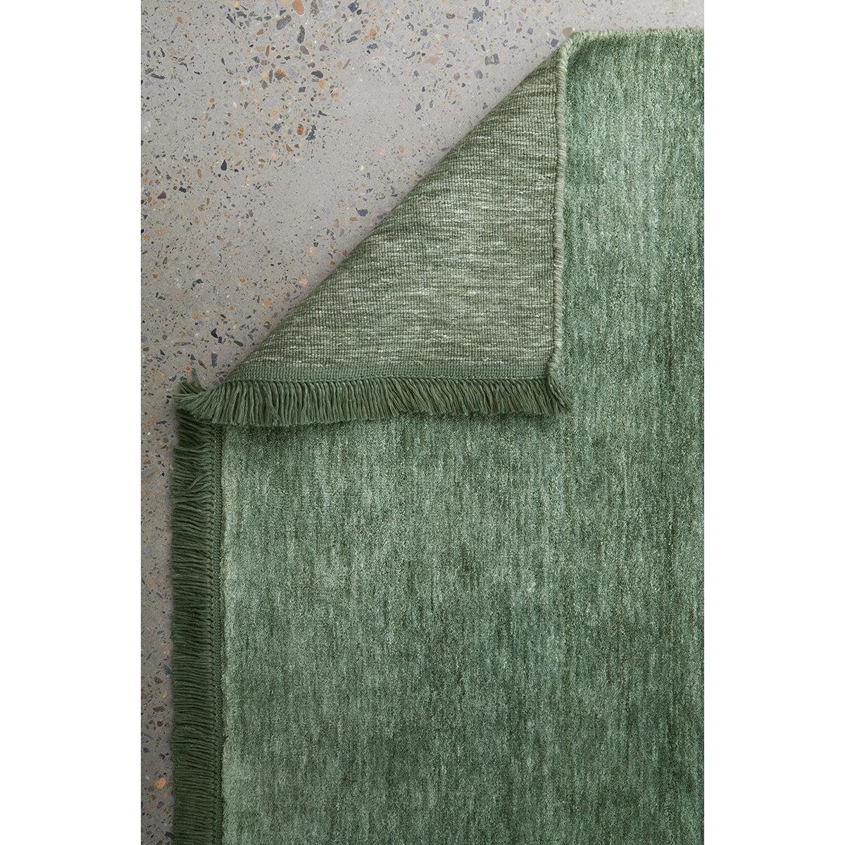 Conscious Loom Kinship Sage Green Rug with textured solid pattern in sage/olive/emerald on grey terrazzo, hand-woven wool